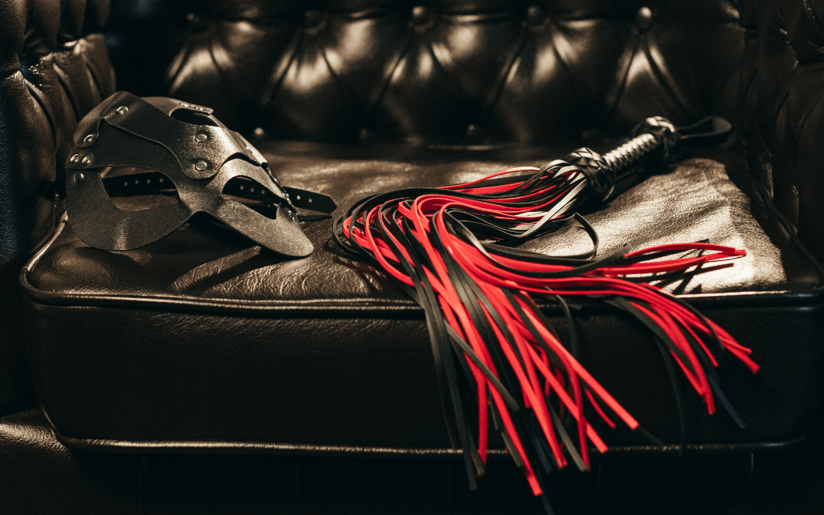 BDSM Mythen Symbolbild: rote Peitsche und Ledermaske auf Ledercouch BDSM myths Symbolic image: red whip and leather mask on leather couch