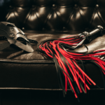 BDSM Mythen Symbolbild: rote Peitsche und Ledermaske auf Ledercouch BDSM myths Symbolic image: red whip and leather mask on leather couch