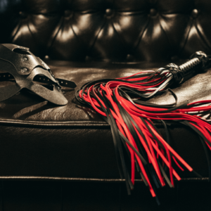 BDSM Mythen Symbolbild: rote Peitsche und Ledermaske auf Ledercouch BDSM myths Symbolic image: red whip and leather mask on leather couch