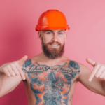 Penis Namen Symbolbild: tätowierter Mann mit freiem Oberkörper deutet nach unten (wo man - nicht auf dem Bild ersichtlich - sein Geschlechtsteil vermutet) / Penis names Symbolic image: tattooed man with bare upper body pointing downwards (where - not visible in the picture - his genitals are assumed to be)