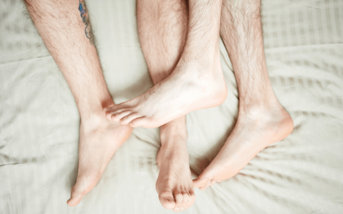 Fußfisting. Symbolbild: 2 Paar Männerfüße im Bett. Englisch: Foot fisting. Symbolic image: 2 pairs of men's feet in bed.