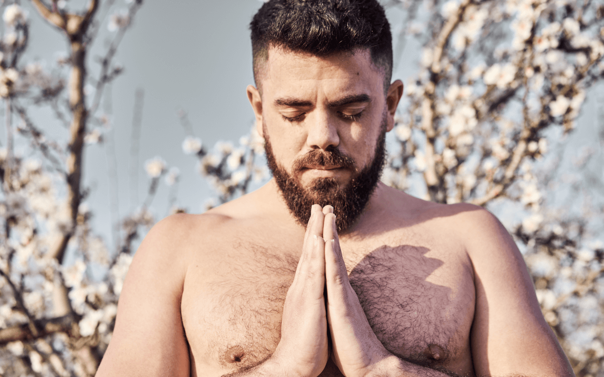 Schwule und Religion. Symbolbild: Mann mit freiem Oberkörper hat die Augen geschlossen und die Hände zum Gebet gefaltet. Englisch: Gay and religious. Symbolic image: Man with bare upper body, eyes closed and hands folded in prayer.