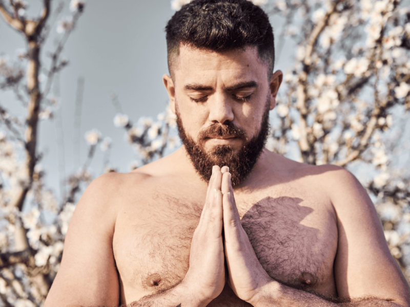 Schwule und Religion. Symbolbild: Mann mit freiem Oberkörper hat die Augen geschlossen und die Hände zum Gebet gefaltet. Englisch: Gay and religious. Symbolic image: Man with bare upper body, eyes closed and hands folded in prayer.