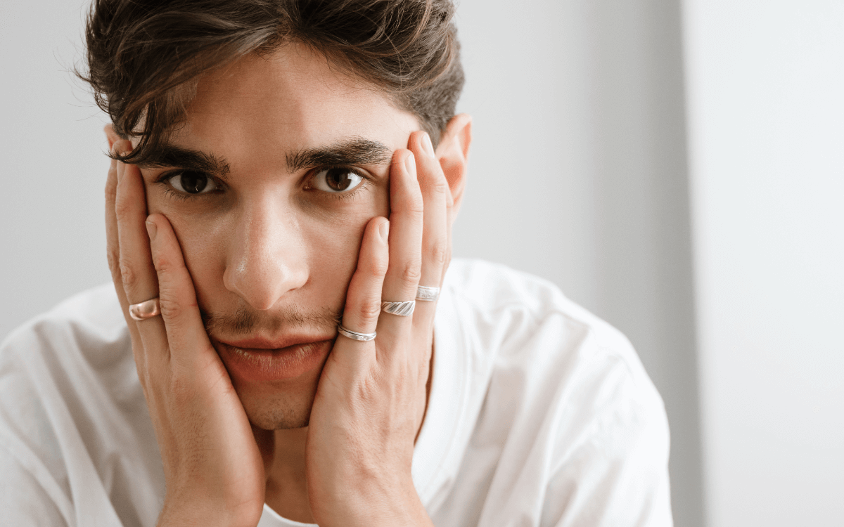 Suizid queere Menschen. Symbolbild: niedergeschlagen dreinblickender Mann hält mit den Händen sein Gesicht. Englisch: Suicide among queer people. Symbolic image: dejected looking man holding his face with his hands