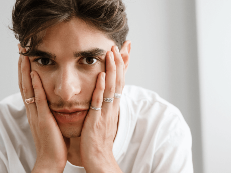 Suizid queere Menschen. Symbolbild: niedergeschlagen dreinblickender Mann hält mit den Händen sein Gesicht. Englisch: Suicide among queer people. Symbolic image: dejected looking man holding his face with his hands