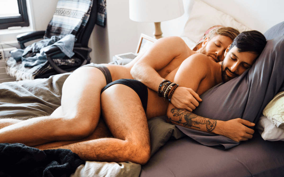 Bottom Sex. Symbolbild: Zwei Männer liegen nur in Unterhose bekleidet auf dem Bett in Löffelchenstellung und kuscheln. Englisch: Bottom sex. Symbolic image: Two men are lying on the bed in spoon position, wearing only their underpants and cuddling.