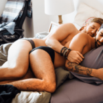 Bottom Sex. Symbolbild: Zwei Männer liegen nur in Unterhose bekleidet auf dem Bett in Löffelchenstellung und kuscheln. Englisch: Bottom sex. Symbolic image: Two men are lying on the bed in spoon position, wearing only their underpants and cuddling.