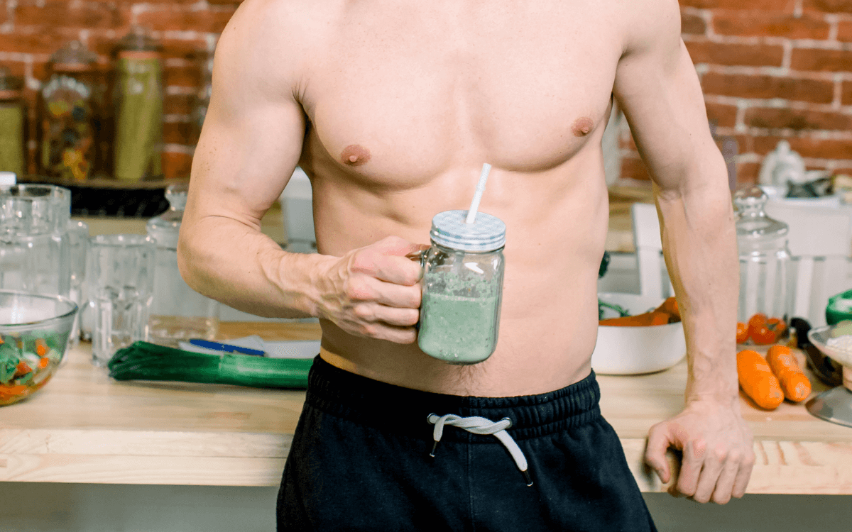 Was sollte ich vor einer Fist-Session essen? Symbolbild: Männlicher, nackter Oberkörper, der einen gesunden, grünen Drink in der Hand hält. Englisch: What should I eat before a fisting session? Symbolic image: Male, naked torso holding a healthy, green drink in his hand.