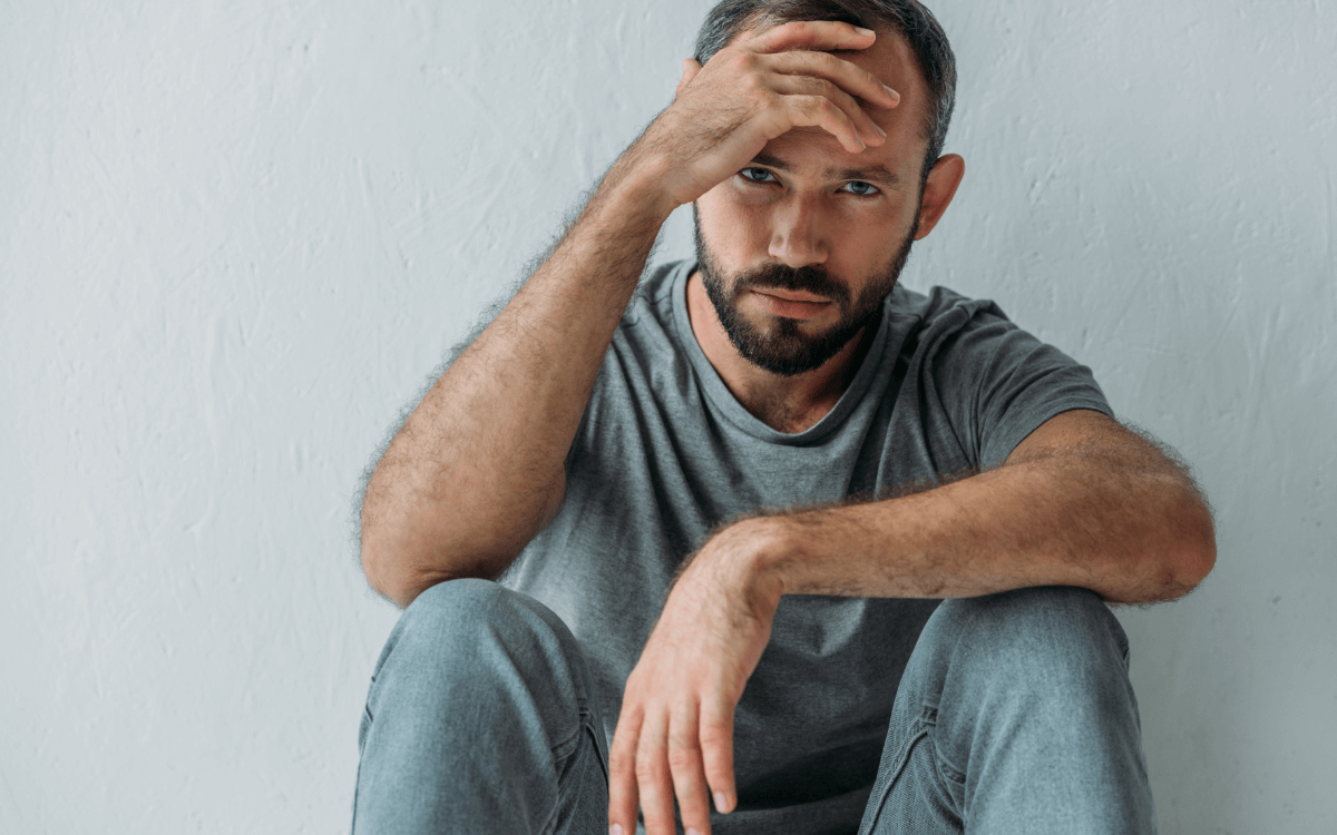 Sucht: Wie Abhängigkeit dein Leben beeinflusst. Symbolbild: Ein Mann sitzt niedergeschlagen da und hält sich die Stirn. Addiction: How addiction can change your life. symbolic image: a man sitting with his hand on his forehead