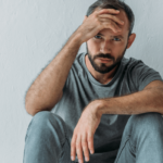 Sucht: Wie Abhängigkeit dein Leben beeinflusst. Symbolbild: Ein Mann sitzt niedergeschlagen da und hält sich die Stirn. Addiction: How addiction can change your life. symbolic image: a man sitting with his hand on his forehead