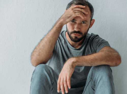 Sucht: Wie Abhängigkeit dein Leben beeinflusst. Symbolbild: Ein Mann sitzt niedergeschlagen da und hält sich die Stirn. Addiction: How addiction can change your life. symbolic image: a man sitting with his hand on his forehead