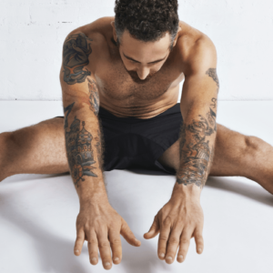 Autofellatio Symbolbild: Ein an den Armen tätowierter Mann, der nur mit Unterhose bekleidet ist, macht Dehnübungen. Englisch: Self-sucking symbol picture: a man tattooed on his arms, wearing only underpants, does stretching exercises.