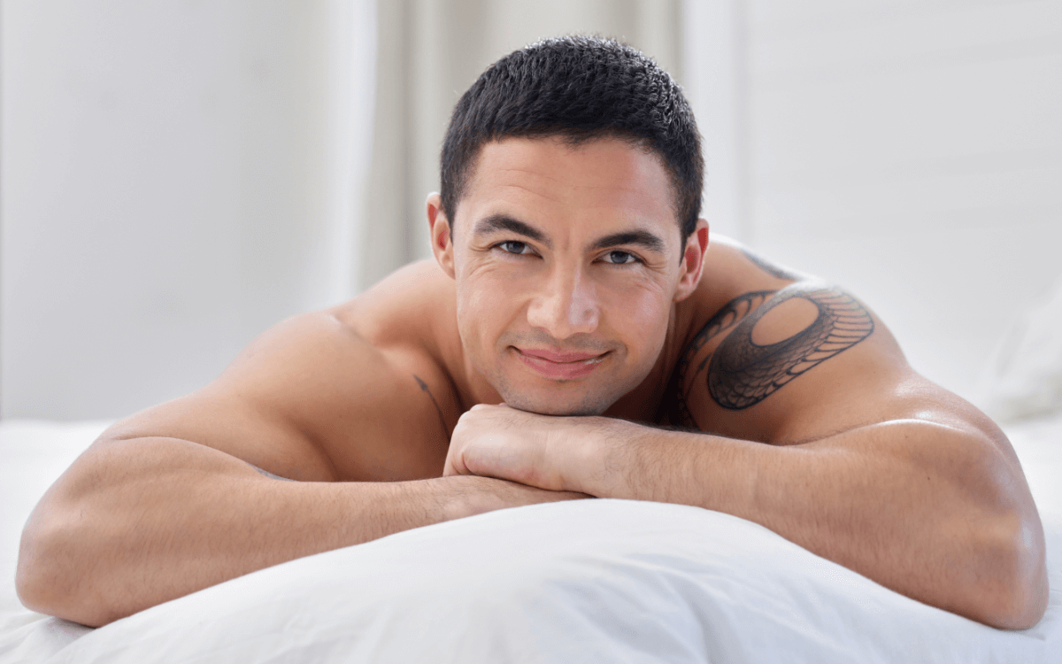 Prostata Massage Symbolbild: Ein Mann mit freiem Oberkörper liegt auf dem Bauch und lächelt in die Kamera. Englisch: Prostate massage, symbolic image: a naked man is lying on his front smiling at the camera.