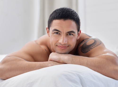 Prostata Massage Symbolbild: Ein Mann mit freiem Oberkörper liegt auf dem Bauch und lächelt in die Kamera. Englisch: Prostate massage, symbolic image: a naked man is lying on his front smiling at the camera.