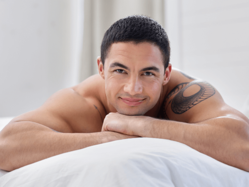 Prostata Massage Symbolbild: Ein Mann mit freiem Oberkörper liegt auf dem Bauch und lächelt in die Kamera. Englisch: Prostate massage, symbolic image: a naked man is lying on his front smiling at the camera.