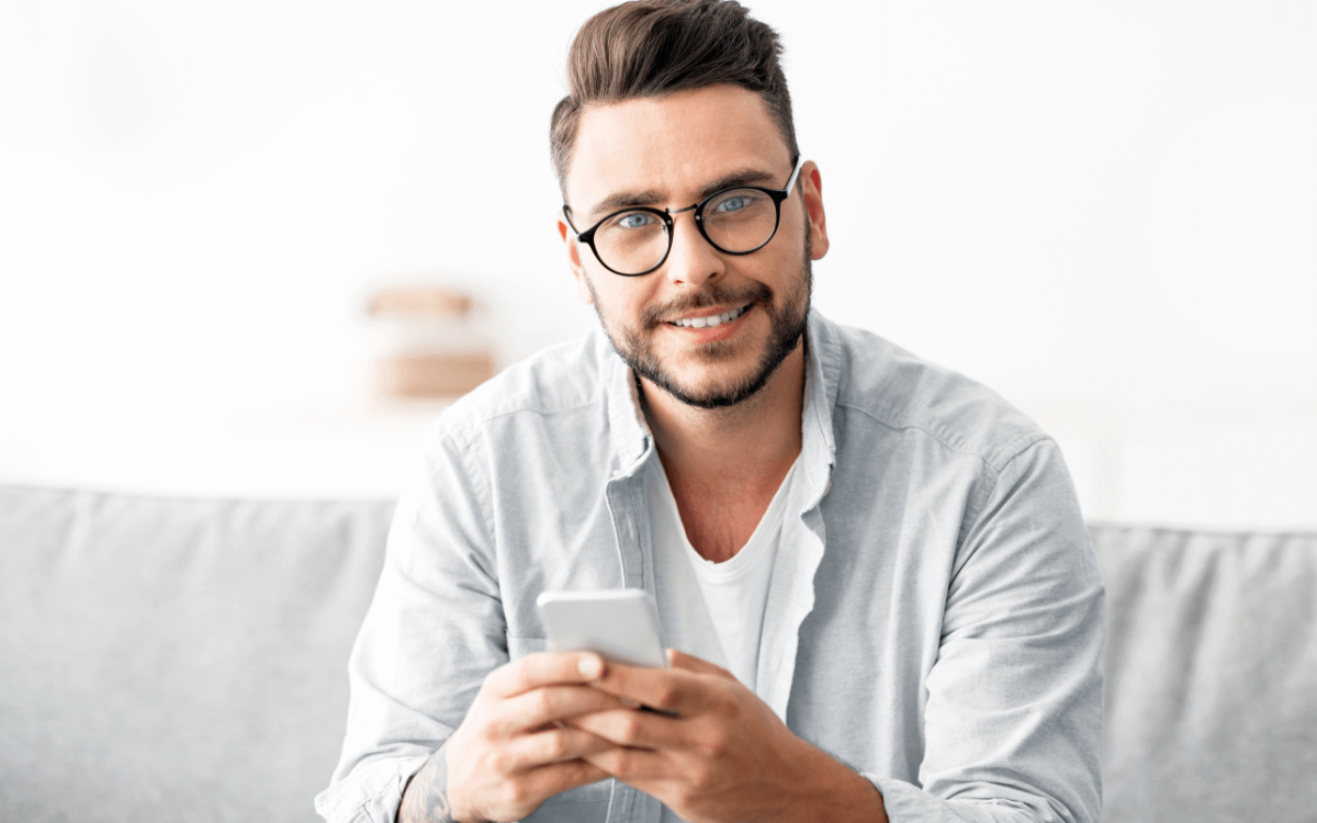 Gesunder Gebrauch einer Dating-App Symbolbild: Ein junger Mann lächelt in die Kamera. Englisch: Healthy use of dating apps. Symbolic image: a young man smiles at the camera.