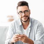 Gesunder Gebrauch einer Dating-App Symbolbild: Ein junger Mann lächelt in die Kamera. Englisch: Healthy use of dating apps. Symbolic image: a young man smiles at the camera.