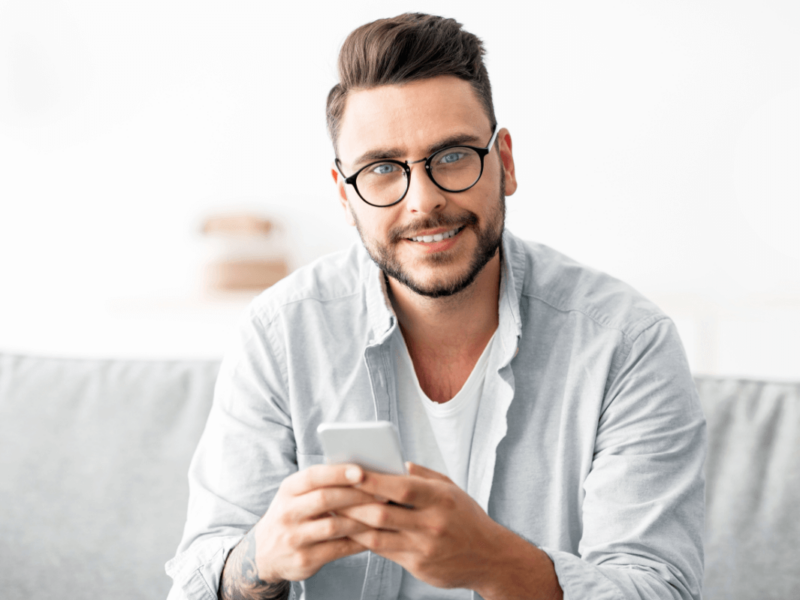 Gesunder Gebrauch einer Dating-App Symbolbild: Ein junger Mann lächelt in die Kamera. Englisch: Healthy use of dating apps. Symbolic image: a young man smiles at the camera.