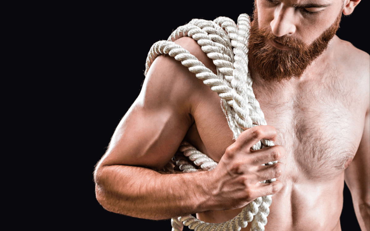 Rigger BDSM oder Rope Top. Symbolbild: Ein Mann mit freiem Oberkörper trägt ein dickes Seil. Englisch: Rigger or rope top. Symbolic image: a shirtless man carries a thick rope.