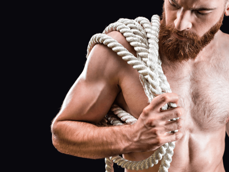 Rigger BDSM oder Rope Top. Symbolbild: Ein Mann mit freiem Oberkörper trägt ein dickes Seil. Englisch: Rigger or rope top. Symbolic image: a shirtless man carries a thick rope.