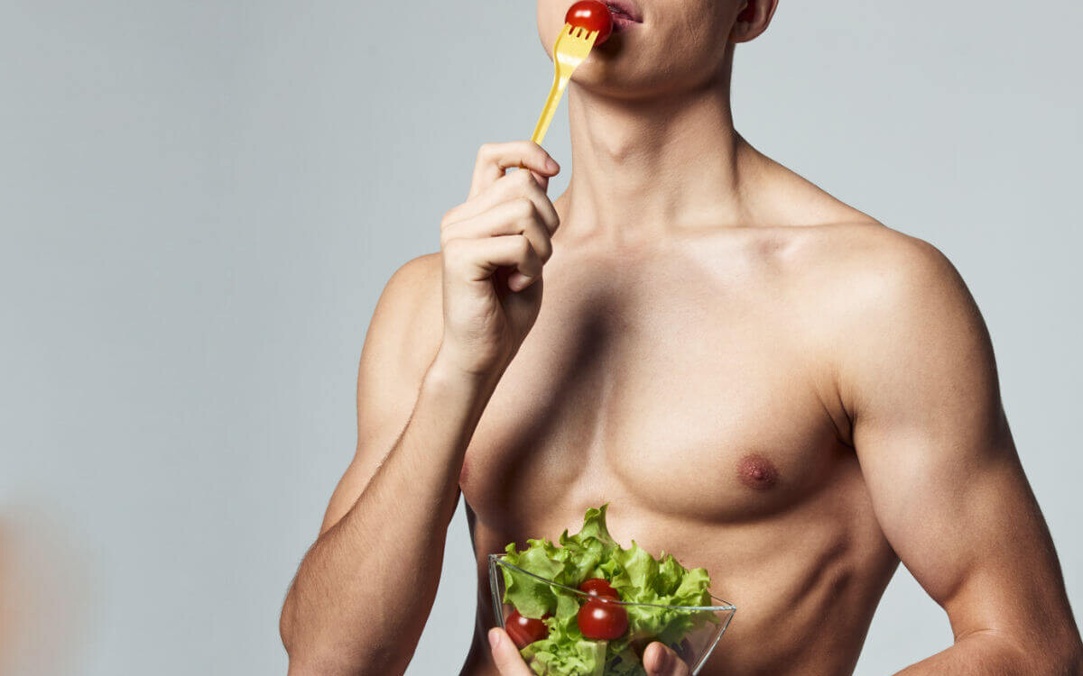 Analsex Vorbereitung Symbolbild: Ein männlicher nackter Oberkörper hält einen Salat in den Händen und führt eine Tomate auf der Gabel zum Mund. Anal sex preparation Symbolic image: A naked male torso holds a salad in his hands and brings a tomato on a fork to his mouth.