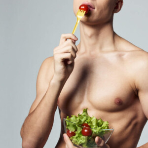 Analsex Vorbereitung Symbolbild: Ein männlicher nackter Oberkörper hält einen Salat in den Händen und führt eine Tomate auf der Gabel zum Mund. Anal sex preparation Symbolic image: A naked male torso holds a salad in his hands and brings a tomato on a fork to his mouth.