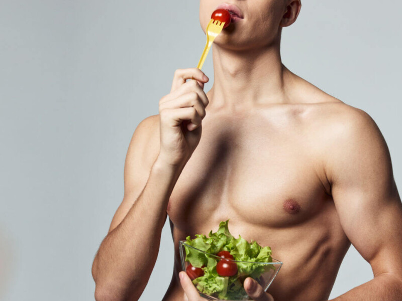 Analsex Vorbereitung Symbolbild: Ein männlicher nackter Oberkörper hält einen Salat in den Händen und führt eine Tomate auf der Gabel zum Mund. Anal sex preparation Symbolic image: A naked male torso holds a salad in his hands and brings a tomato on a fork to his mouth.