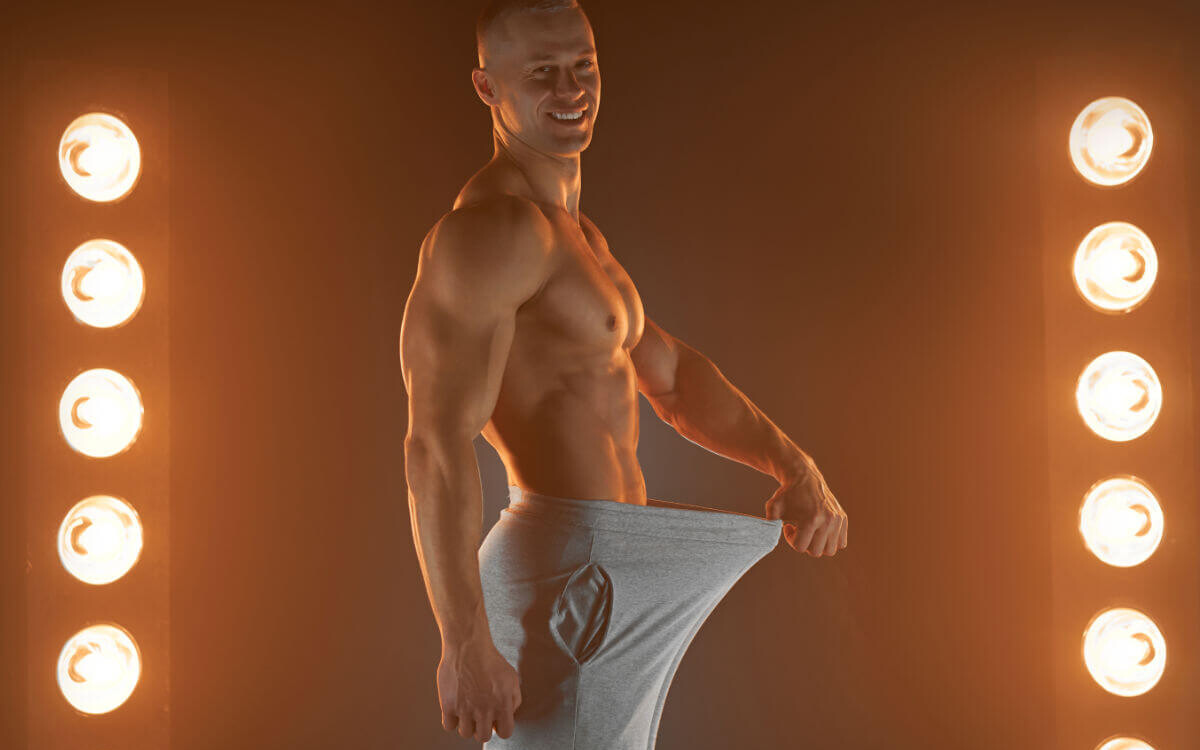Penislänge Symbolbild: Ein Mann mit nacktem Oberkörper hält seine Hose im Schritt soweit von sich weg, dass ein langer Penis angedeutet wird. Englisch: Penis length Symbolic image: A man with a bare upper body holds his pants away from his crotch, suggesting a long penis.