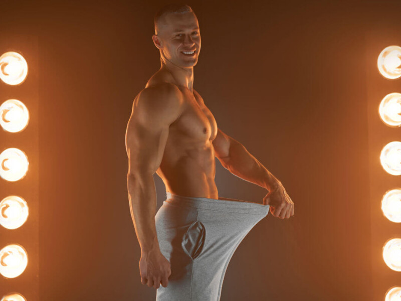 Penislänge Symbolbild: Ein Mann mit nacktem Oberkörper hält seine Hose im Schritt soweit von sich weg, dass ein langer Penis angedeutet wird. Englisch: Penis length Symbolic image: A man with a bare upper body holds his pants away from his crotch, suggesting a long penis.