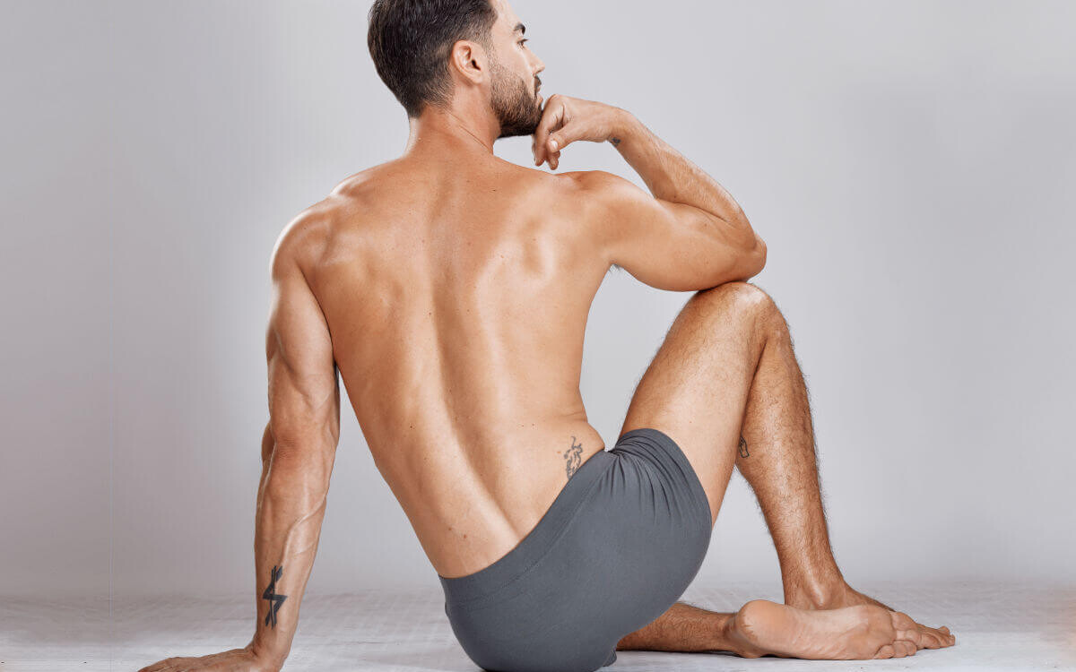 Prostatamassage Symbolbild: Ein Mann, nur mit Unterhose bekleidet, sitzt mit dem Rücken zur Kamera auf dem Boden. Englisch: Prostate massage Symbolic image: A man wearing only underwear is sitting on the floor with his back to the camera.
