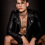 Fetisch vs. Kink Symbolbild: Ein Mann mit offener Lederjacke und Zigarre im Mund schaut lassziv in die Kamera. Fetish vs. Kink Symbolic image: A man with an open leather jacket and a cigar in his mouth looks lasciviously into the camera.