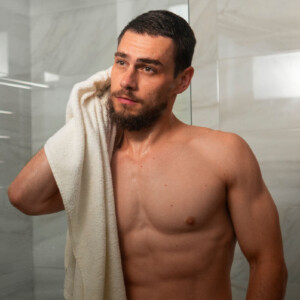 Analsex Reinigung Symbolbild: ein Mann kommt aus der Dusche und trocknet sich mit dem Handtuch ab. Englisch: Anal sex cleaning Symbolic image: a man comes out of the shower and dries himself with a towel.