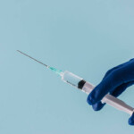 Spritze in den Penis. Symbolbild: Eine Hand mit medizinischem Handschuh hält eine Spritze. Englisch: Penis Injection. Symbolic image: A hand wearing a medical glove holding a syringe.