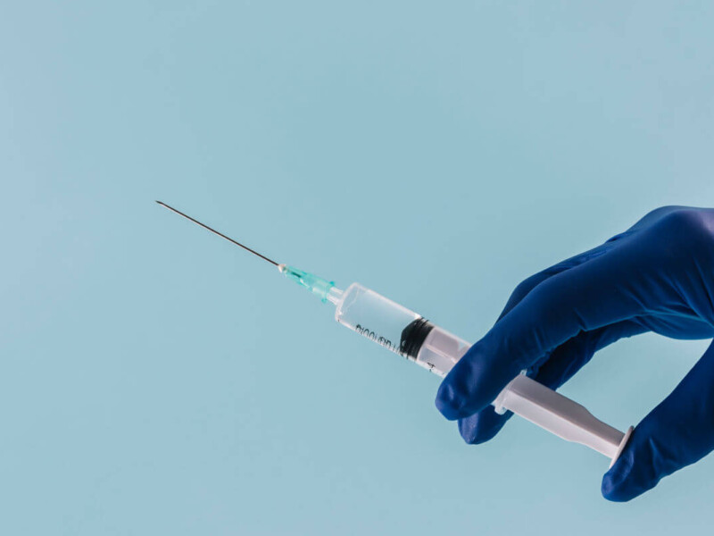 Spritze in den Penis. Symbolbild: Eine Hand mit medizinischem Handschuh hält eine Spritze. Englisch: Penis Injection. Symbolic image: A hand wearing a medical glove holding a syringe.
